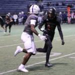 Two high school football players in uniform and helmets practice on a field